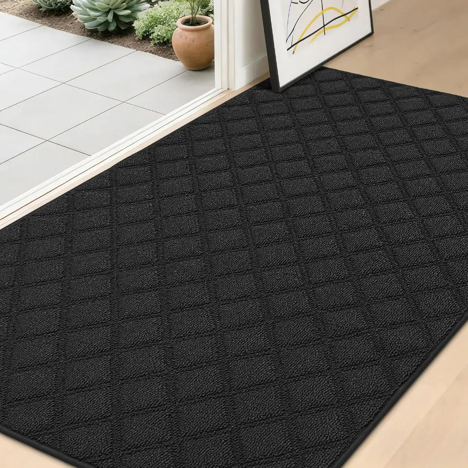 Black textured mat on a wooden floor with a white wall and plants in the background