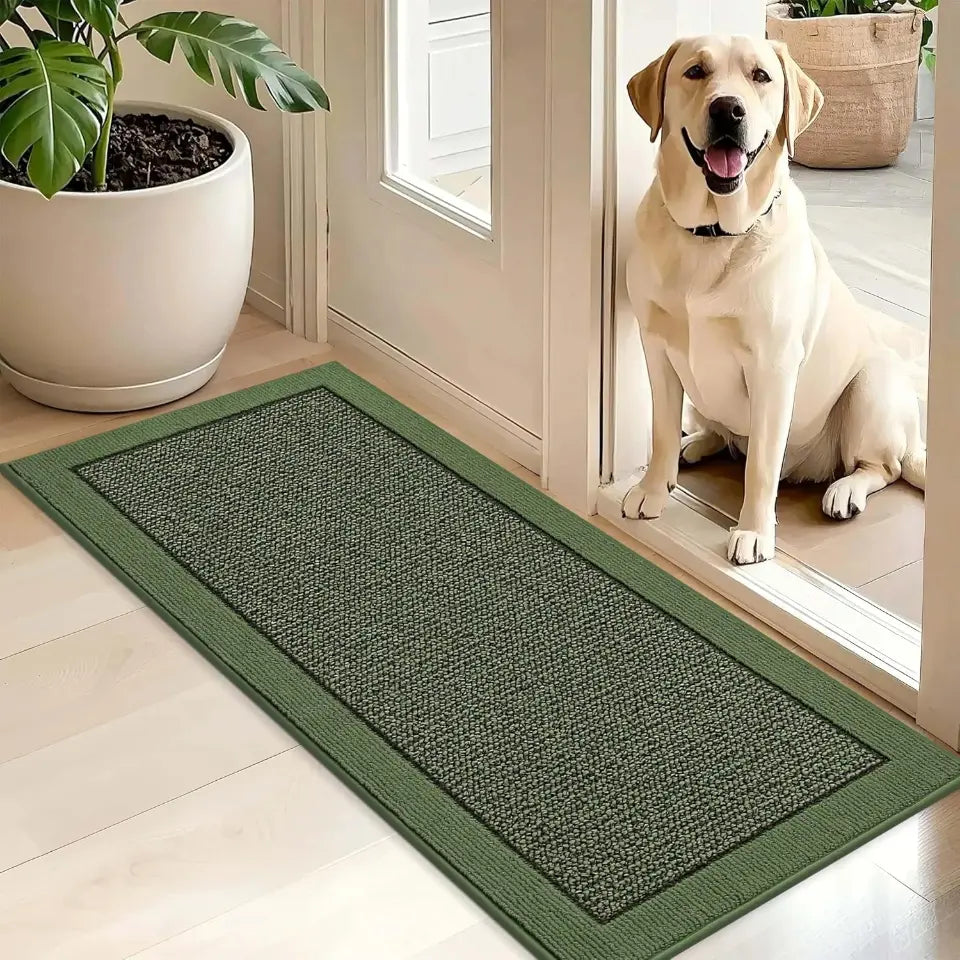 Green doormat on a wooden floor with a dog sitting inside a house.