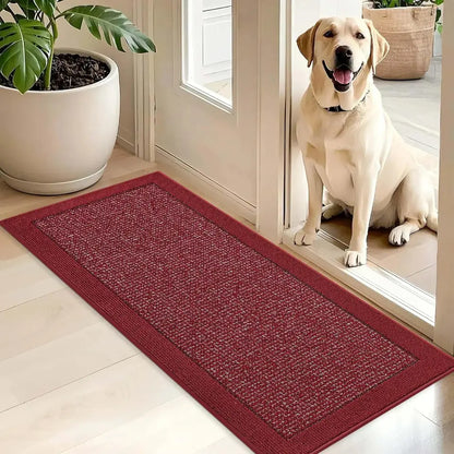 Dog sitting on a red doormat inside a house with a plant in the background.